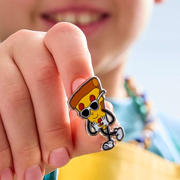 A close-up of the Cool Pizza Pin, which is being hold by a young boy wearing a yellow apron.