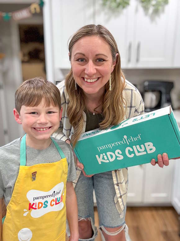 A mom holding and her daughter posing next to a plate of beignets while holding a Kids Club box.